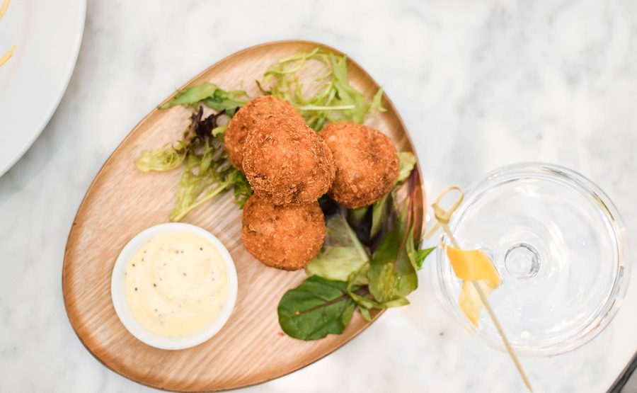 Arancini served on a wooden board with aioli and lemon