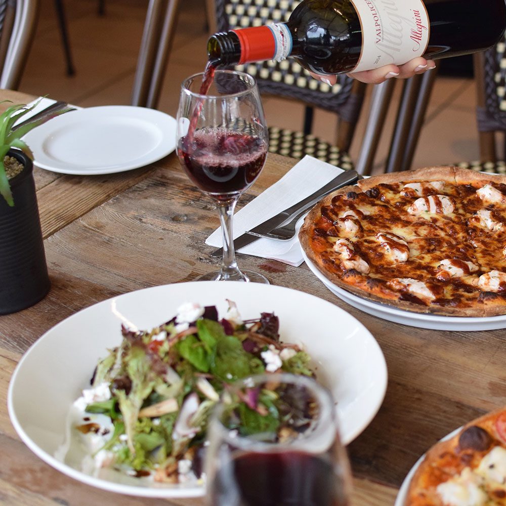 A table set with pizza, salad and a glass of red wine being poured